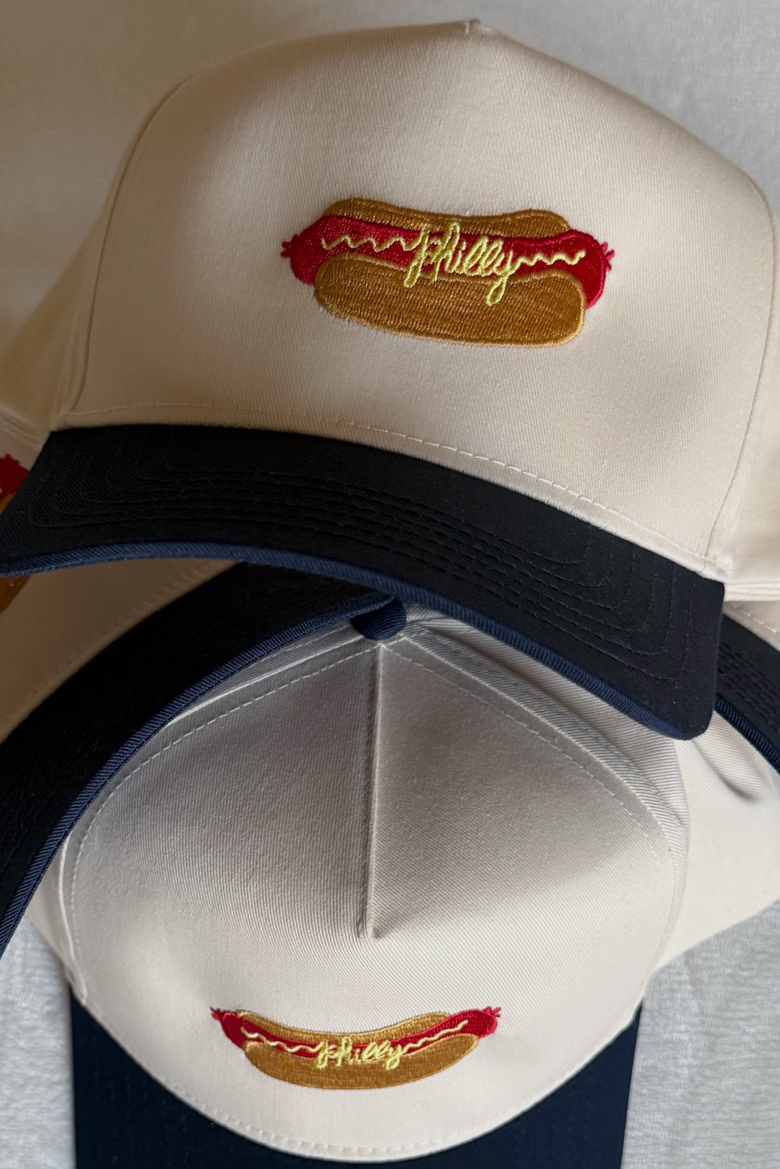 Two baseball caps with hot dog graphic and 'Philly' text on a gray background